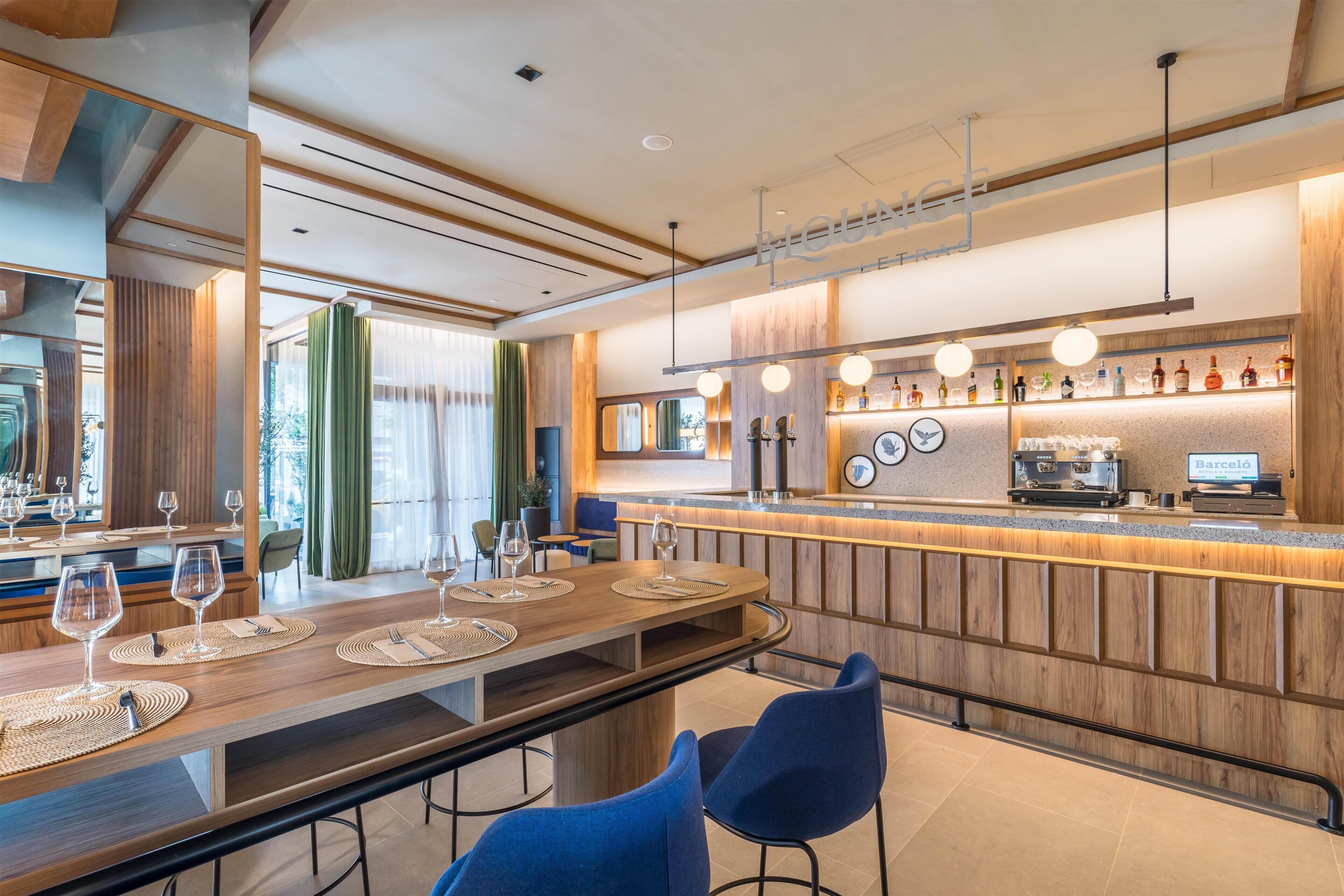 A modern bar area with a wooden counter, bar stools, and a variety of bottles and glasses.
