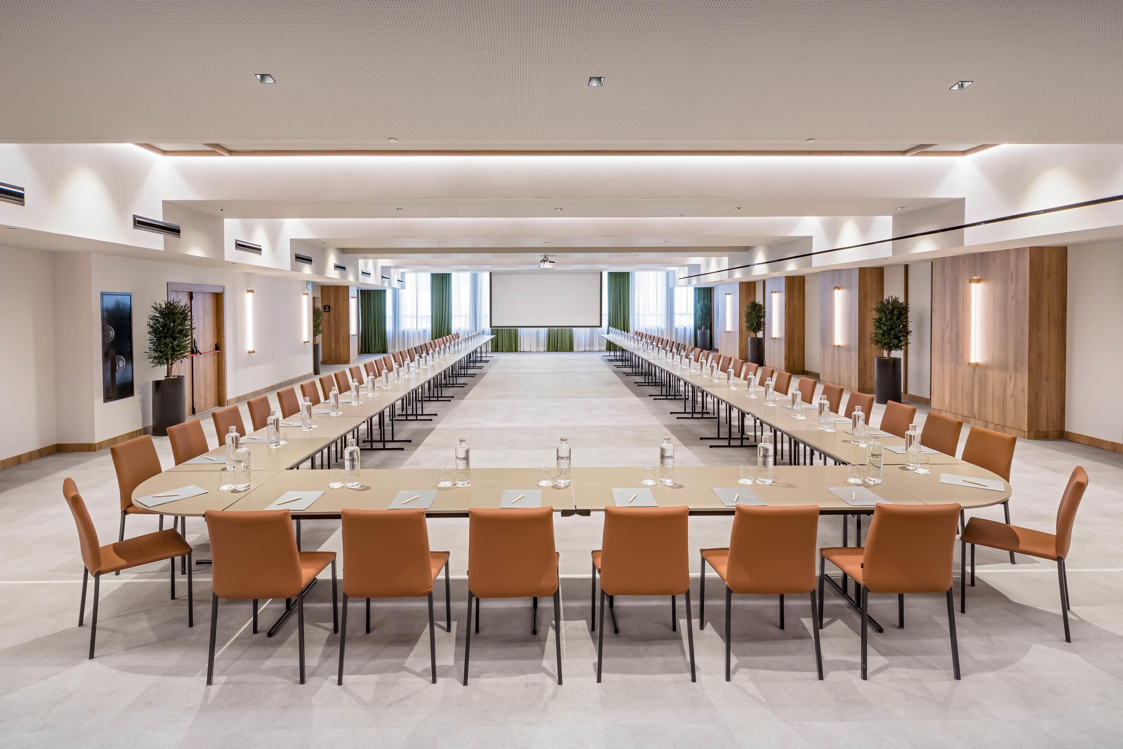 Una sala de conferencias con una larga mesa, sillas y una pantalla para proyector.