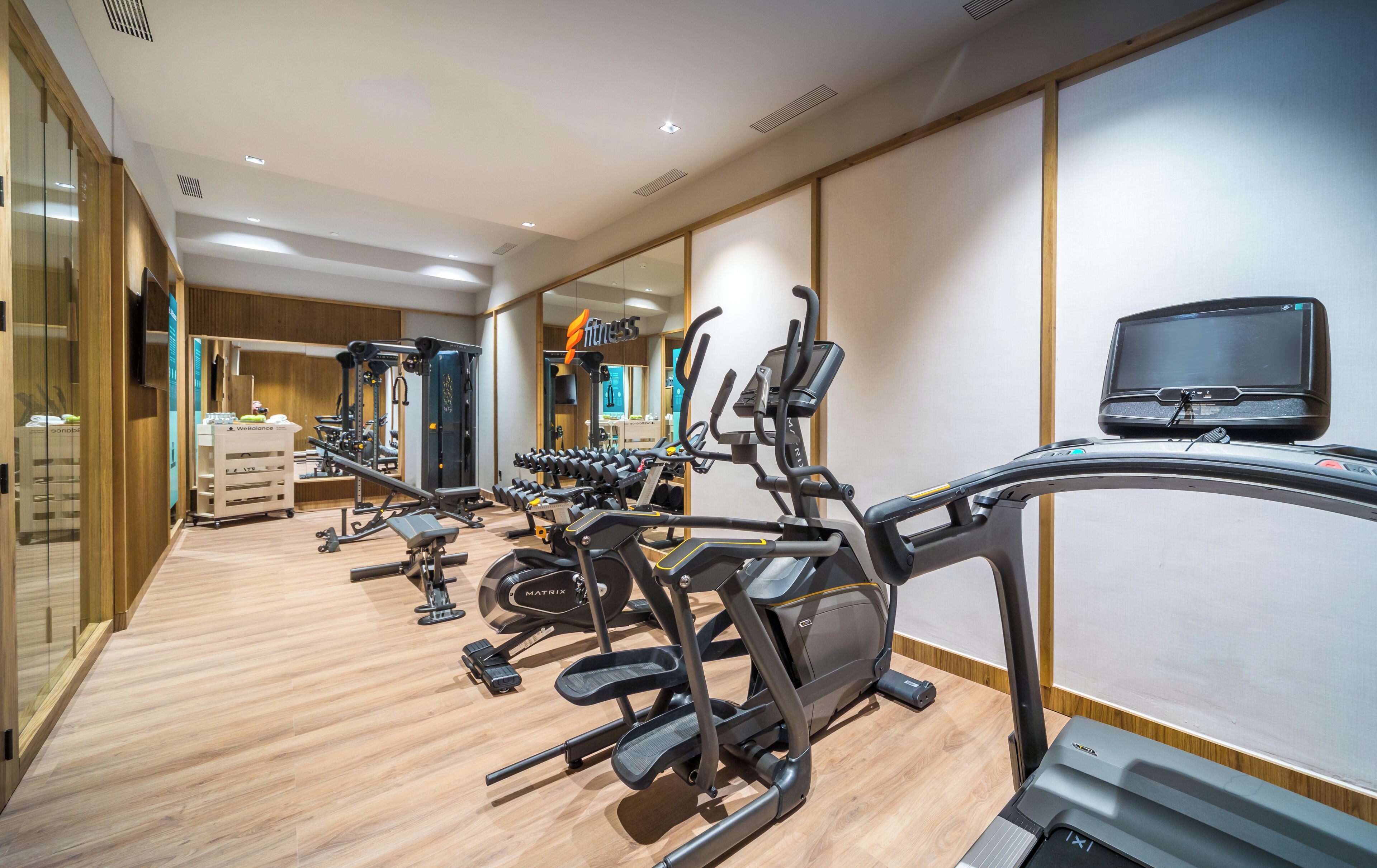 Un gimnasio con cintas de correr, máquinas de pesas y un espejo grande.