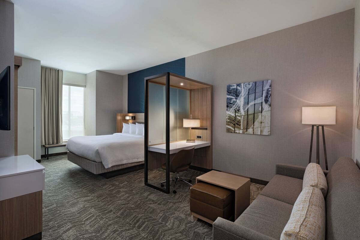 A hotel room with a bed, desk, chair, sofa, and a TV.