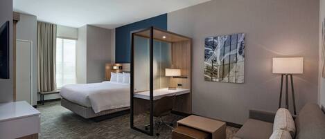 Ein Hotelzimmer mit Bett, Schreibtisch, Stuhl, Sofa und Fernseher.