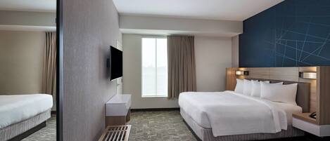 A hotel room with a large bed, a TV mounted on the wall, a window with curtains, and a patterned carpet.