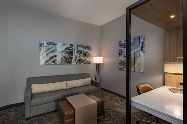 A hotel room with a grey sofa, a small table, and two wall-mounted paintings. - Springhill Suites by Marriott Waco (Waco)