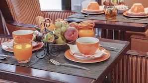 A breakfast setting with a table set for two, including plates, cups, a basket of fruits, and a teapot. - Hotel Vaneau Saint Germain (Paris)