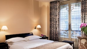 A hotel room with a large bed, two bedside lamps, a small table with a radio, and a view through a patterned window. - Hotel Vaneau Saint Germain (Paris)