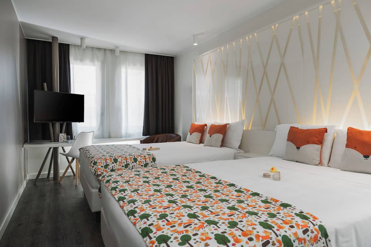 Une chambre d’hôtel avec deux lits, un bureau, une télévision et une grande fenêtre avec des rideaux.