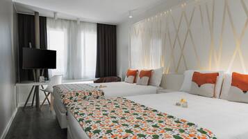 Habitación de hotel con dos camas, un escritorio, un televisor y un ventanal con cortinas.