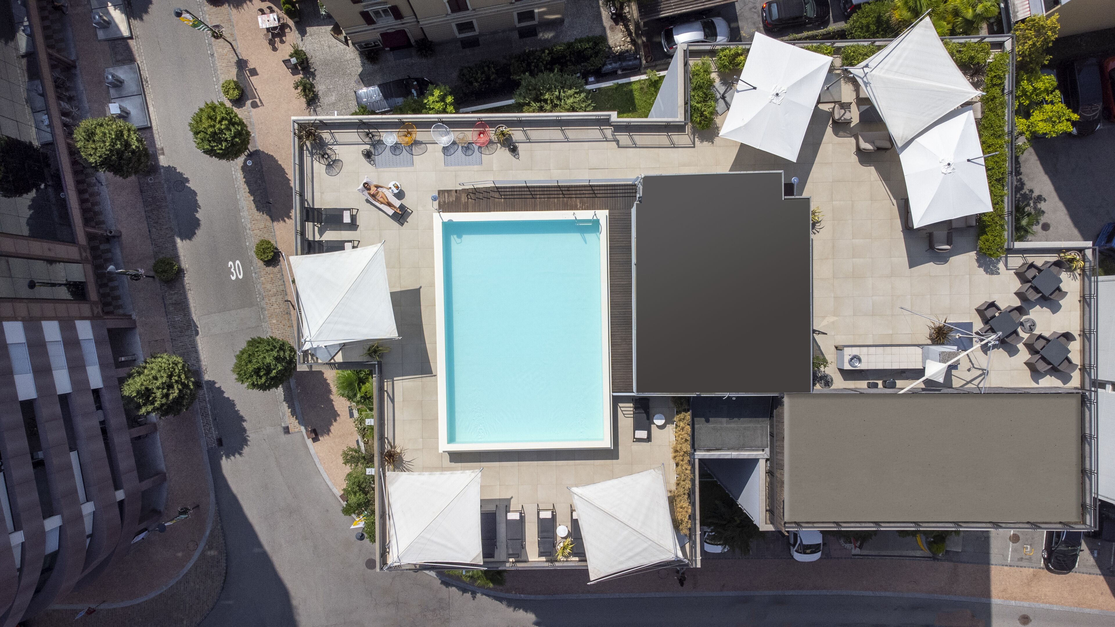 An aerial view of a rooftop pool area with a rectangular pool, surrounded by outdoor seating and umbrellas.