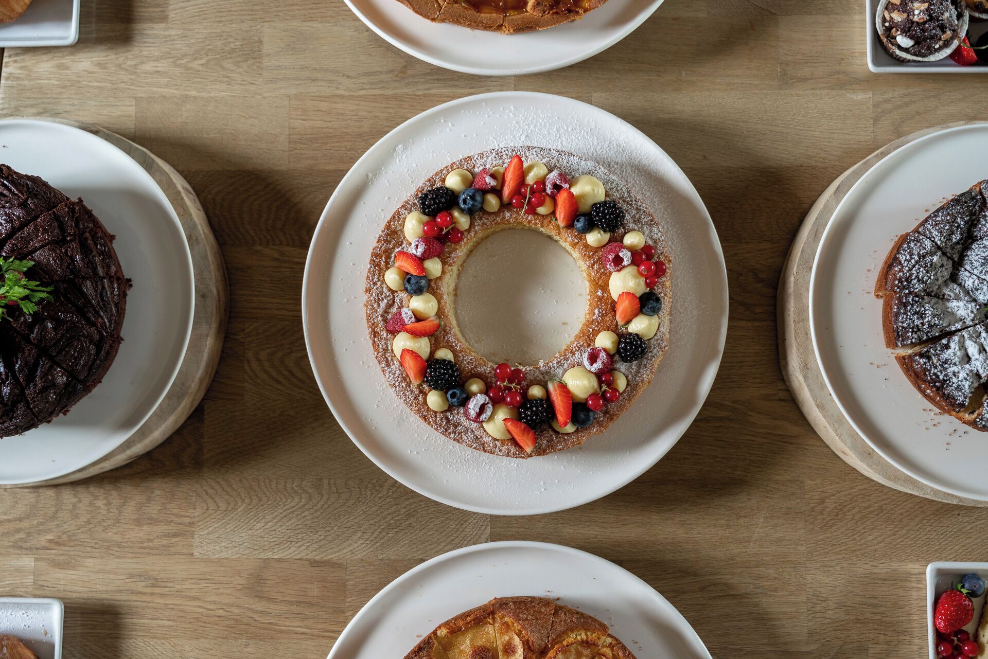 Vista cenital de una mesa de comedor con varios platos de comida, incluyendo un pastel con frutas y un pastel de chocolate.