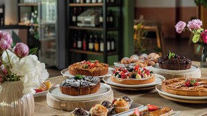 Variedad de postres sobre una mesa, incluyendo pasteles y productos de pastelería, con una estantería de vinos al fondo.
