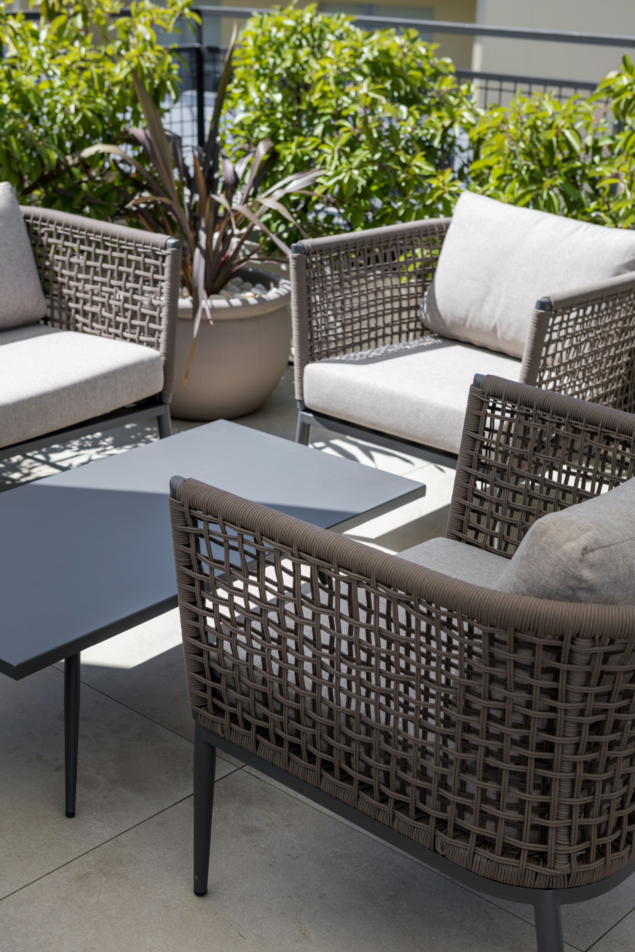 Muebles de mimbre con cojines, una mesa y plantas en macetas en un patio exterior.