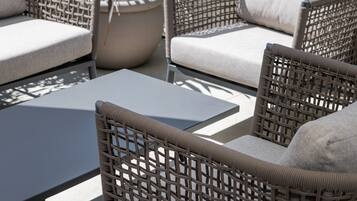 Muebles de mimbre con cojines, una mesa y plantas en macetas en un patio exterior.