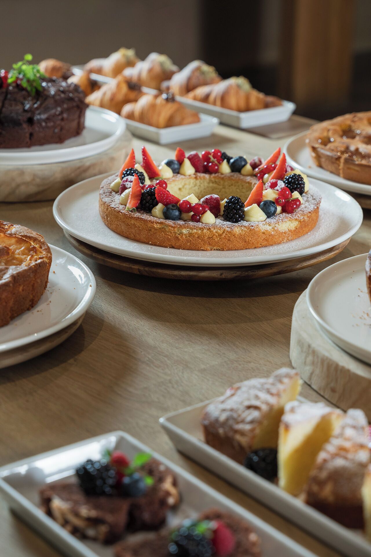 Une variété de desserts est présentée sur la table, notamment une tarte garnie de fruits, des pâtisseries et d’autres douceurs.