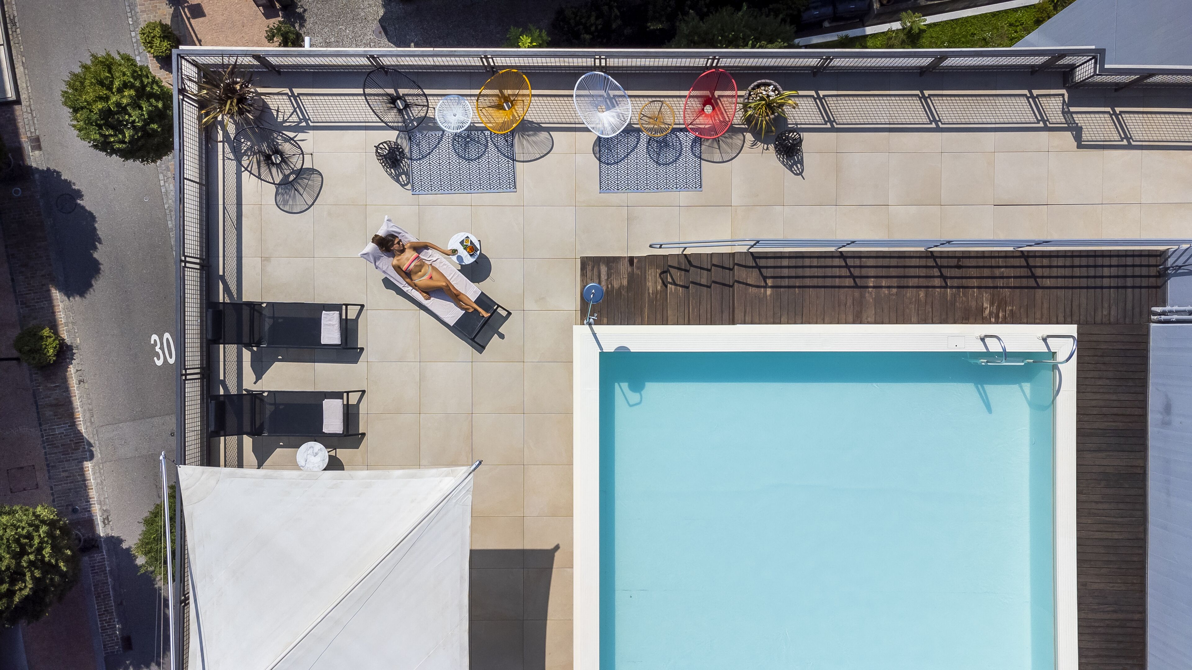 Vista aérea de un área de piscina en la azotea con sillones, sombrillas y una piscina.