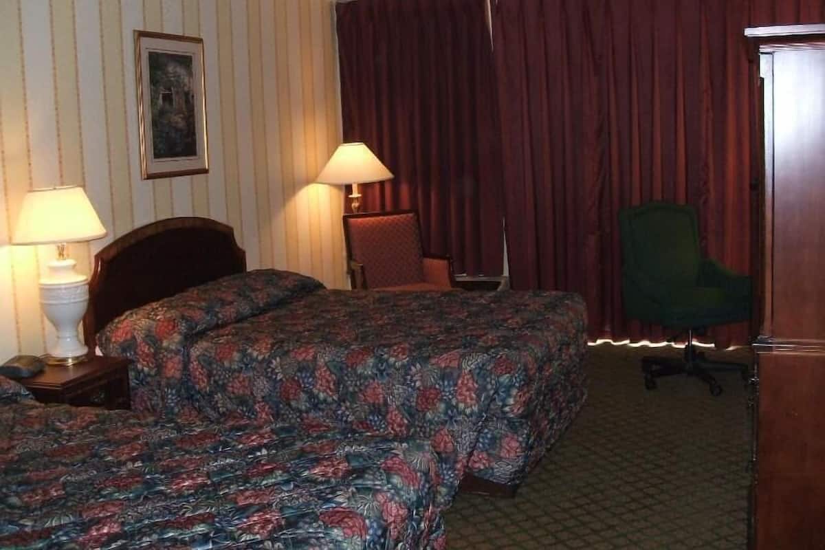 A hotel room with two beds, a desk, a chair, and a lamp.