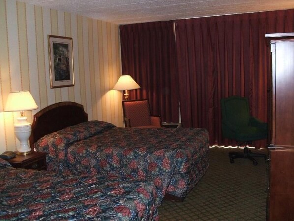 Habitación de hotel con dos camas, un escritorio, una silla y una lámpara.