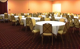 Un salón de conferencias con varias mesas redondas y sillas, suelo alfombrado y un telón de fondo.