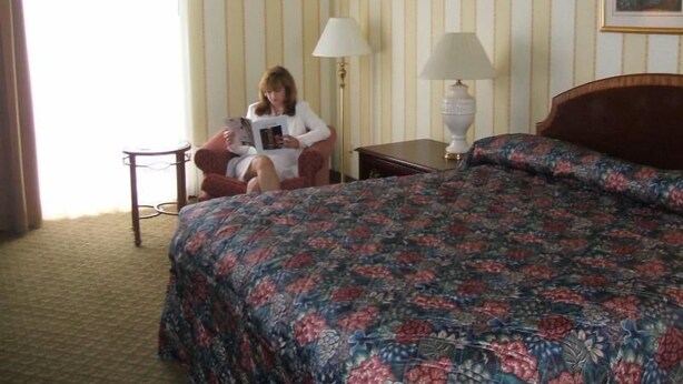 A hotel room with a bed, a chair, a lamp, and a window with curtains. - A Victory Inn & Suites - Ann Arbor (Ann Arbor)