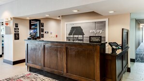 Una recepción con un mostrador, una pantalla digital, un cuadro de una playa y un cartel que dice 'enjoy'.