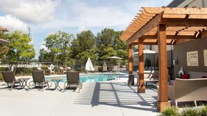 Zona de piscina con sillones reclinables, una pérgola de madera y un cartel que indica que no hay socorrista de servicio.