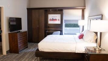 A hotel room with a bed, a dresser, a desk, a television, and a window with a cityscape view.