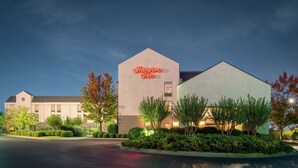 Un hotel Hampton Inn con diseño moderno, que destaca un llamativo letrero de neón, jardines bien cuidados y un amplio estacionamiento.