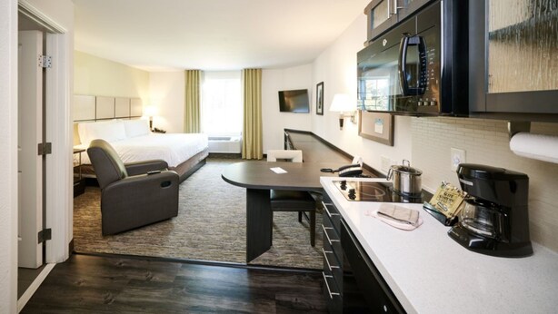A hotel room with a bed, a desk, a kitchenette, and a TV.