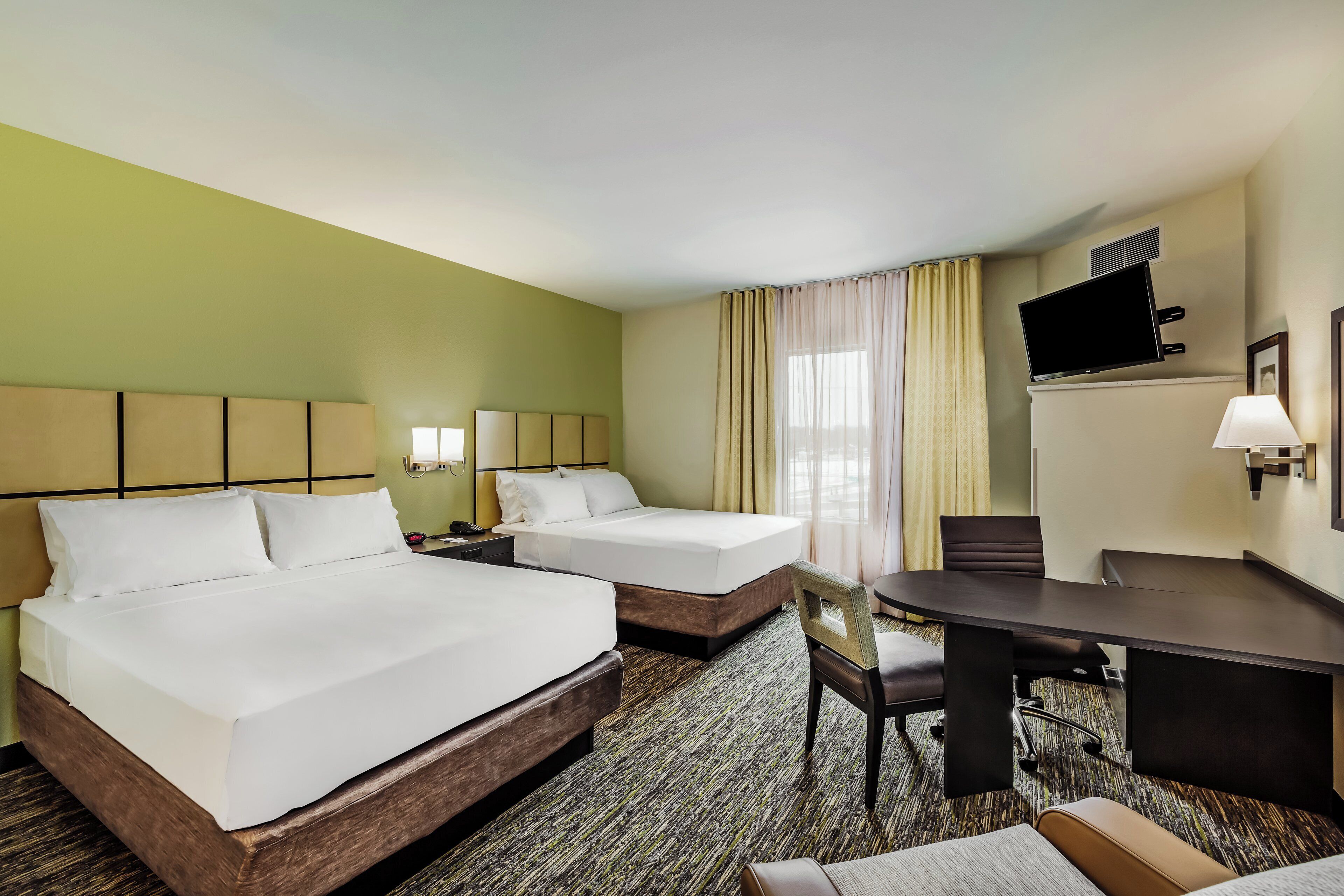 A hotel room with two beds, a desk, a chair, a TV, and a window with curtains.