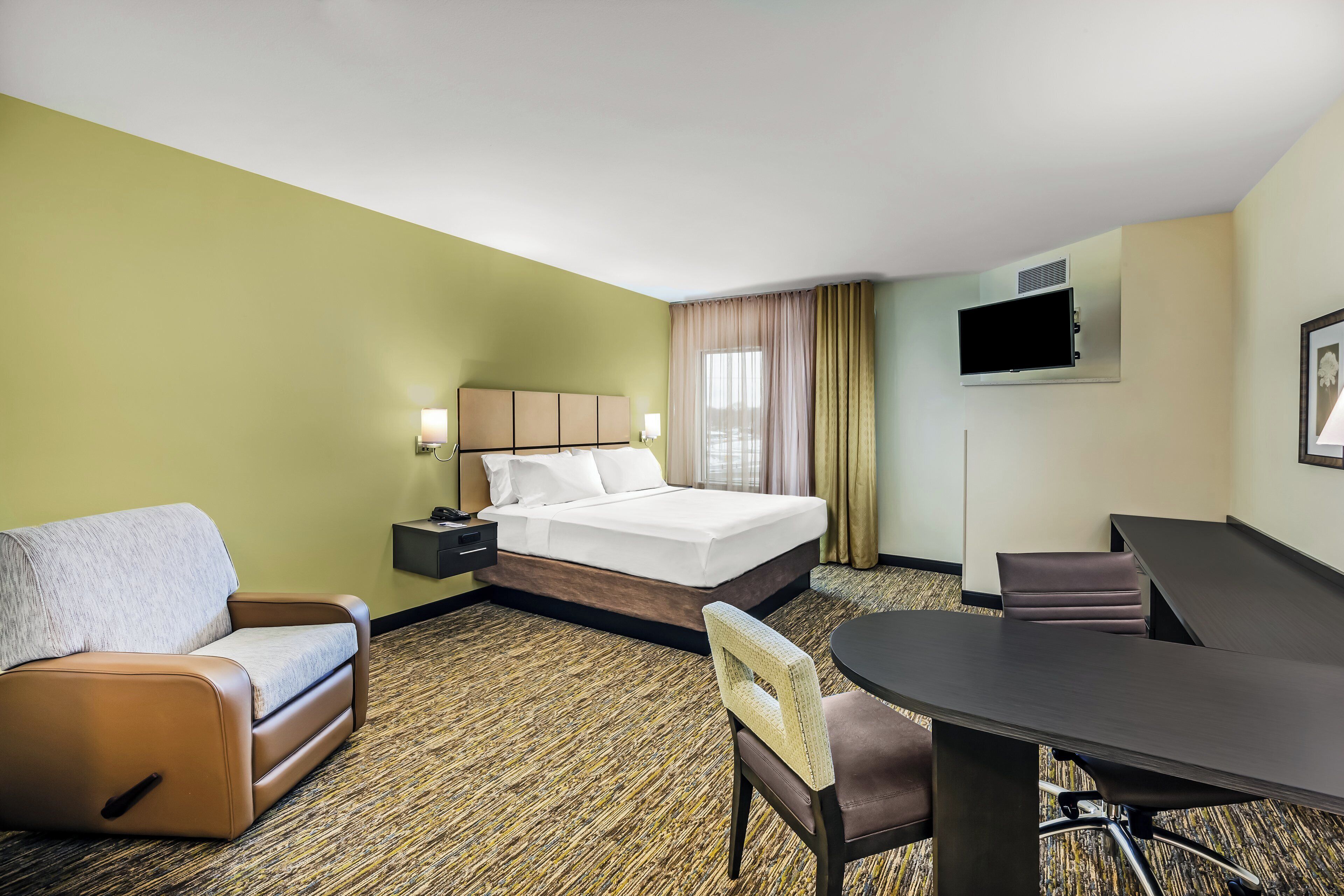 A hotel room with a bed, a desk, a chair, a sofa, and a television.