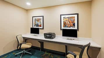 A conference room with two desks, each with a computer monitor, keyboard, and mouse. There are two framed artworks on the wall above the desks.