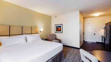 Habitación de hotel con una cama grande, un escritorio, una silla, una mesita, un cuadro en la pared y una puerta que da a la cocina.