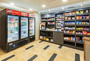 Un espacio para bebidas y aperitivos, con dos refrigeradores, estantes llenos de bocadillos y un microondas.
