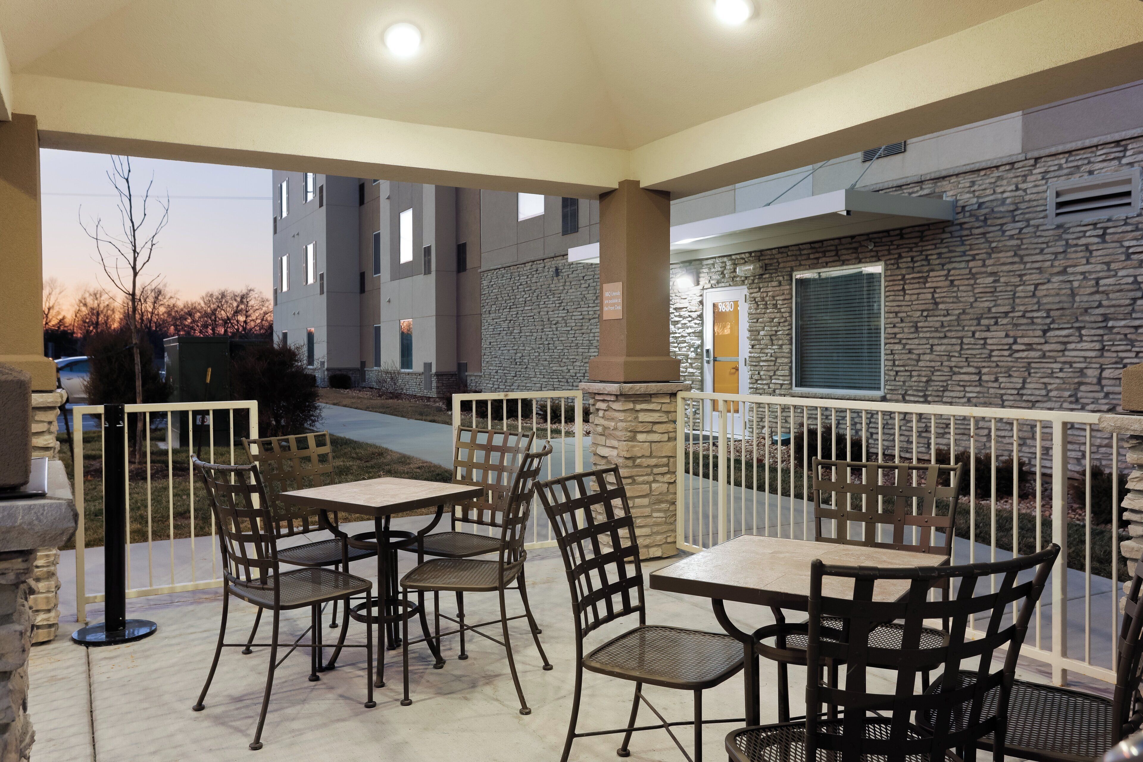 An outdoor patio area with tables and chairs, a stone wall, and a view of a building in the background.