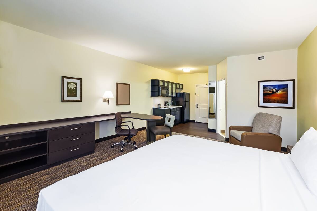 Een hotelkamer met een bed, bureau, stoel, kitchenette en een deur naar een andere kamer.
