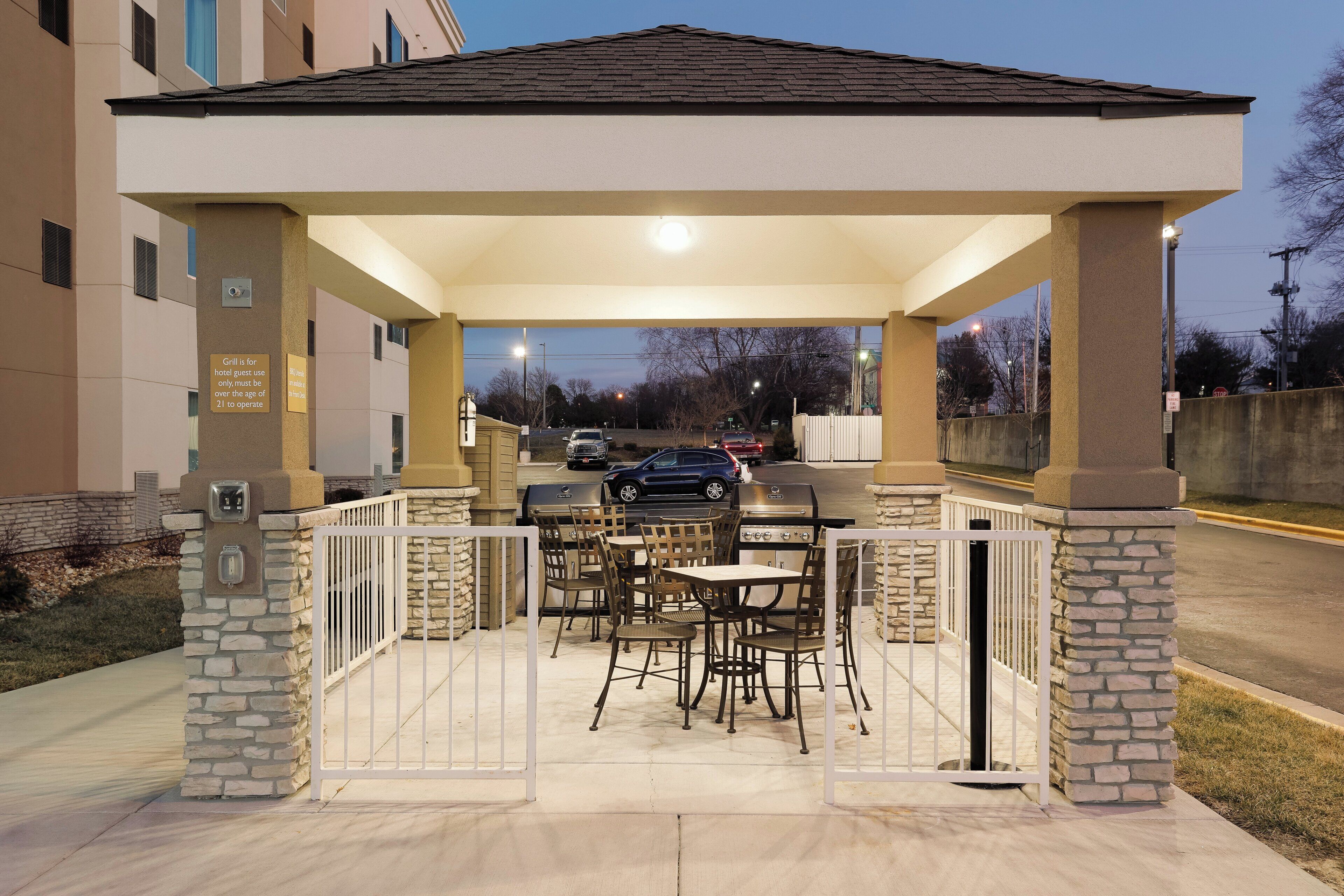 An outdoor patio with a covered seating area, a grill, and a view of the street.
