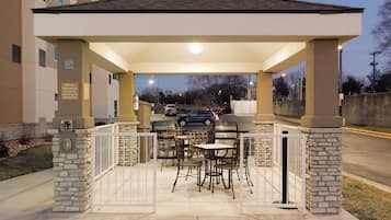 Un patio exterior con zona de estar techada, una parrilla y vistas a la calle.