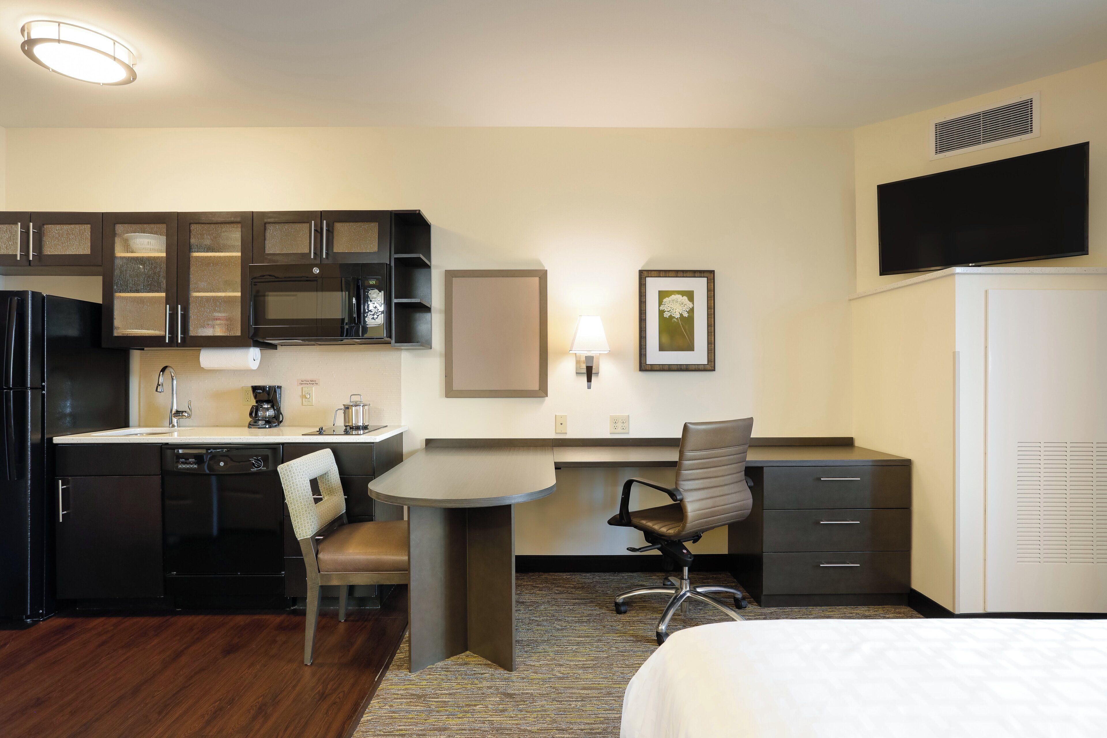 A compact hotel room with a kitchenette, a bed, a desk, and a chair.