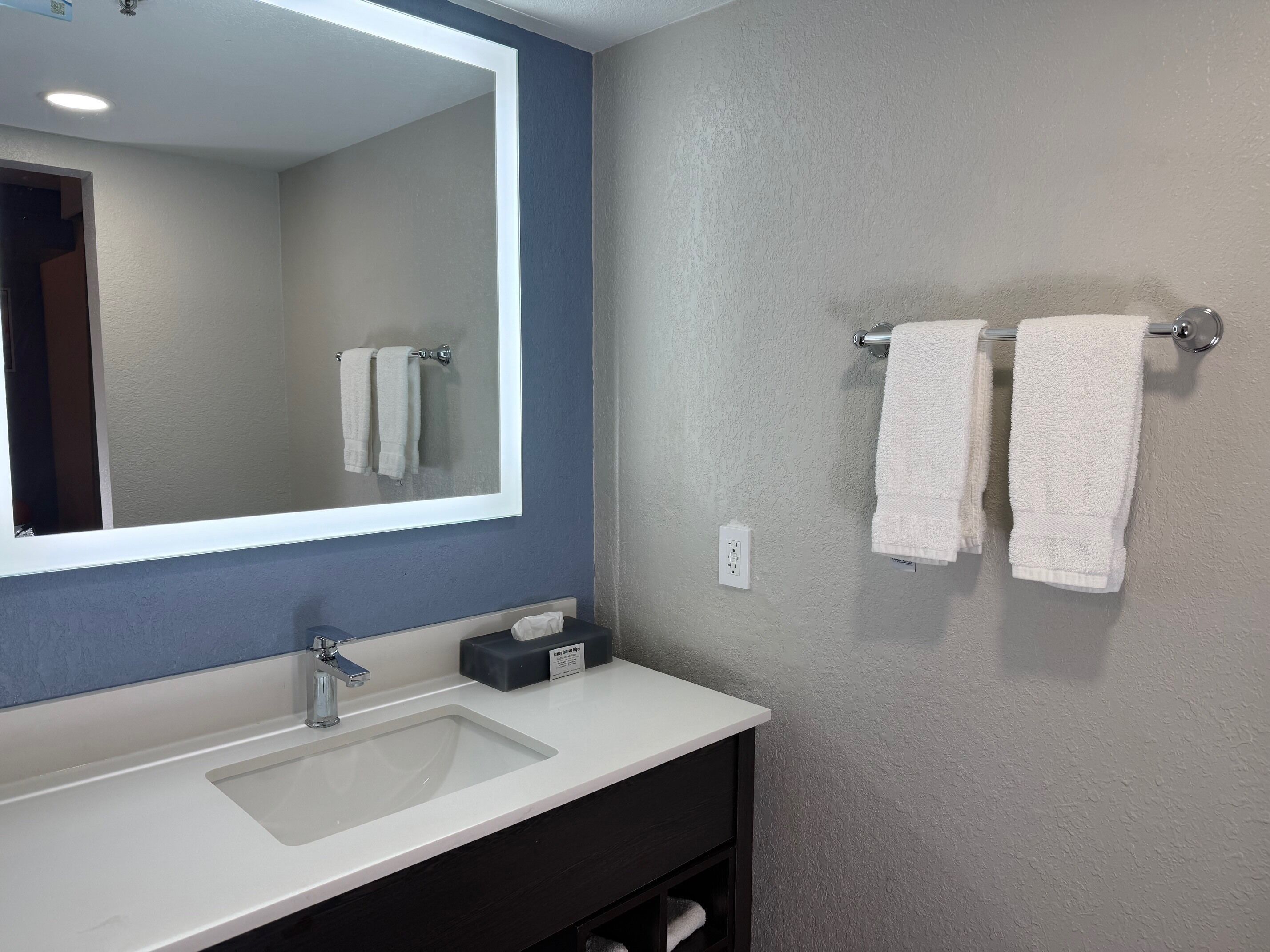 A bathroom with a white sink, a mirror, and two towels hanging on a towel rack.