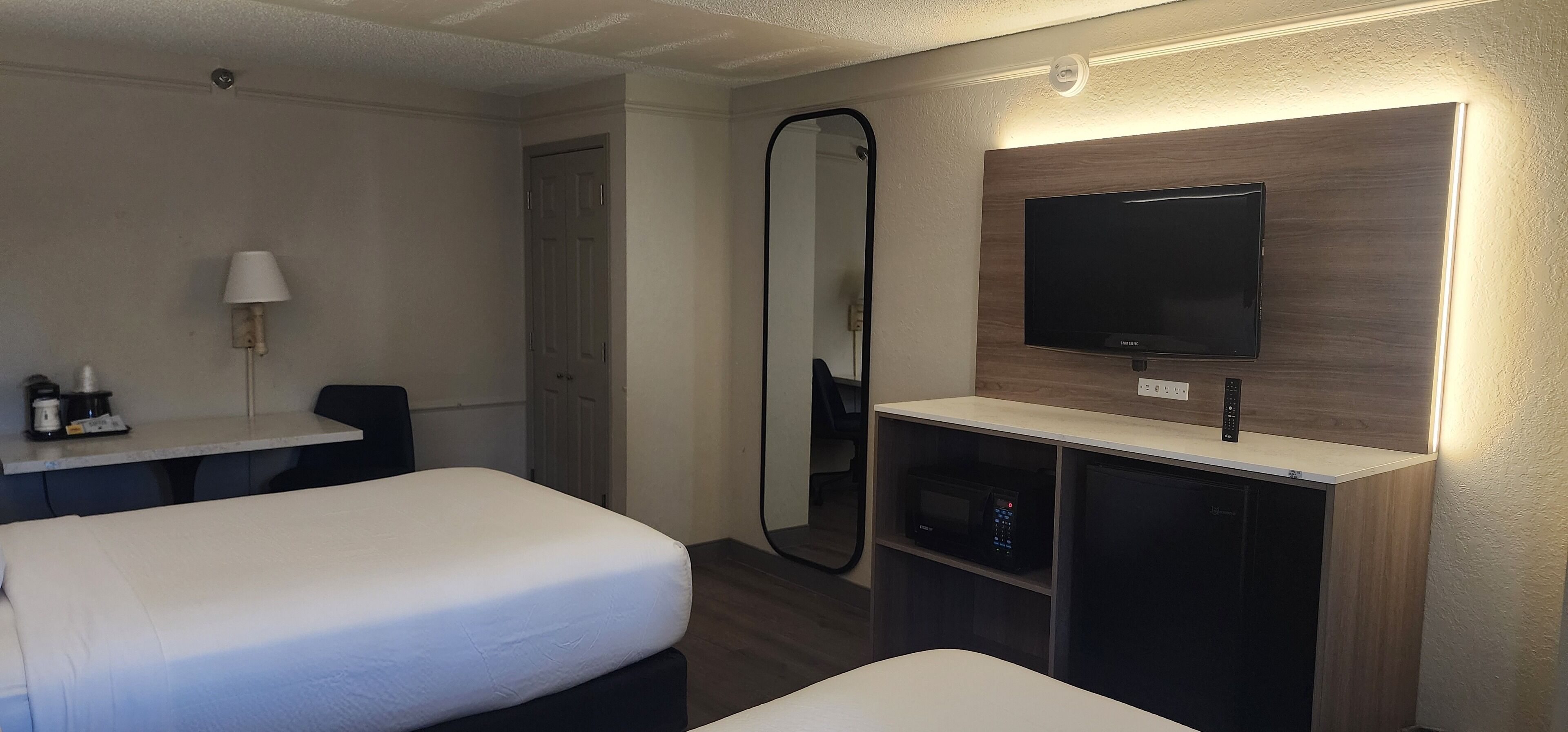Habitación de hotel con dos camas, un escritorio, un televisor, un espejo y un minibar.