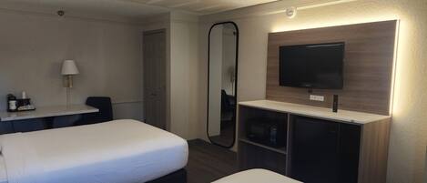 Habitación de hotel con dos camas, un escritorio, un televisor, un espejo y un minibar.