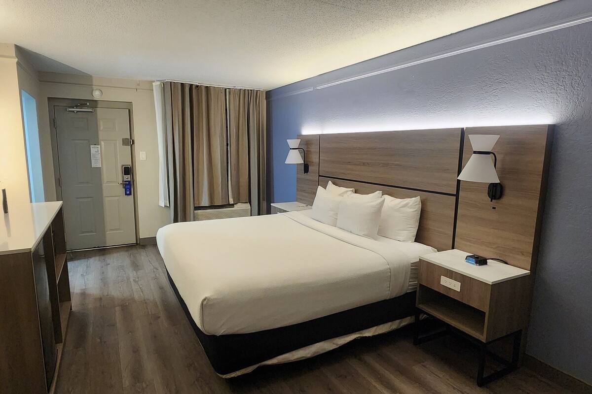 Ein Hotelzimmer mit Bett, Nachttischen, Fernseher, Vorhängen und einer Tür.