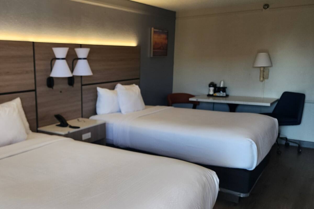 Ein Hotelzimmer mit zwei Betten, einem Schreibtisch, einem Stuhl und einer Lampe.