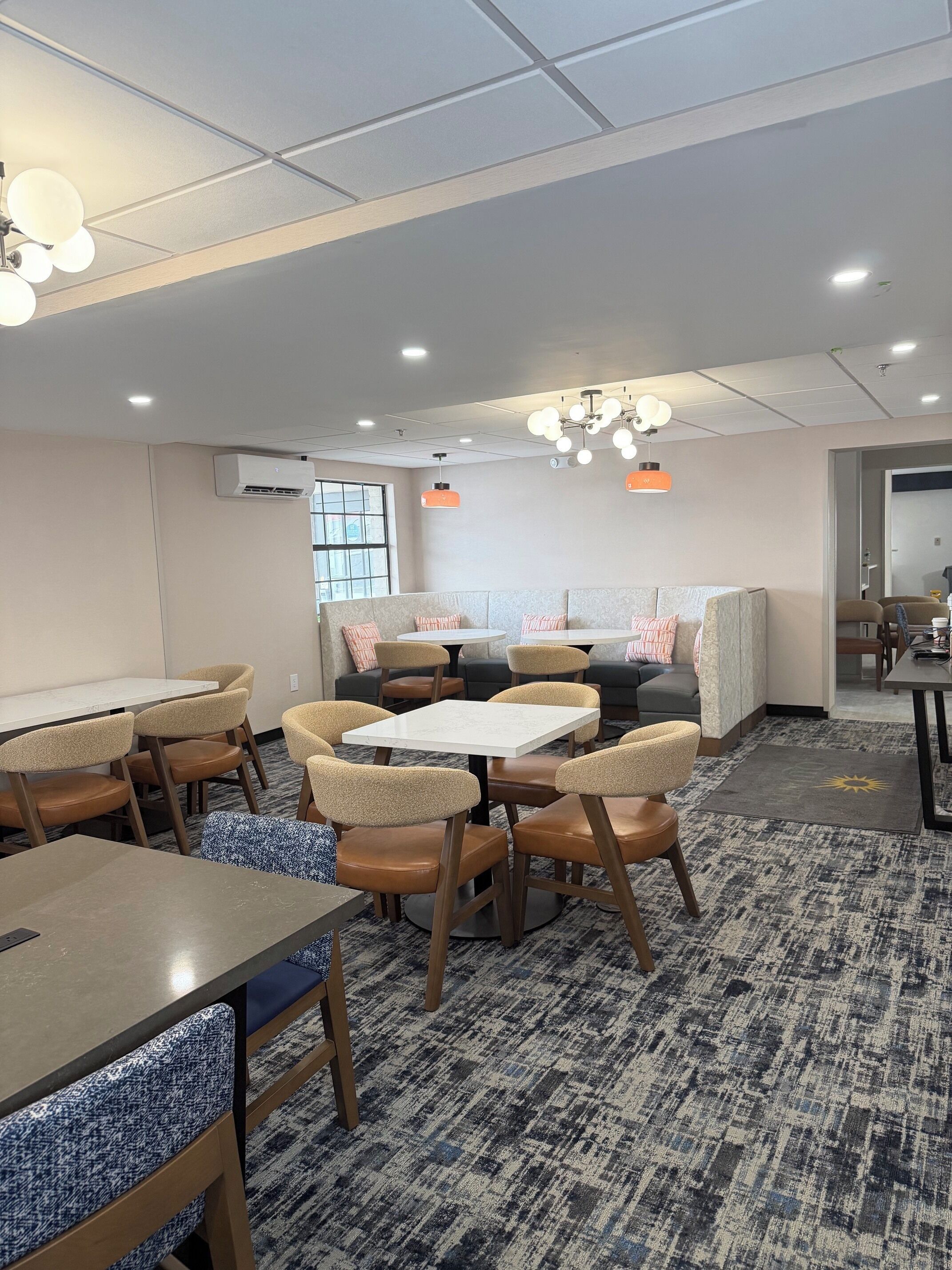 A modern hotel room with a sofa, dining table, chairs, and a patterned carpet.