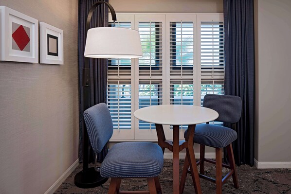 Una habitación con una mesa redonda, dos sillas a rayas, una lámpara y una ventana con persianas.