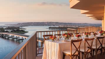 A dining table set for six with chairs, overlooking a body of water and a bridge.