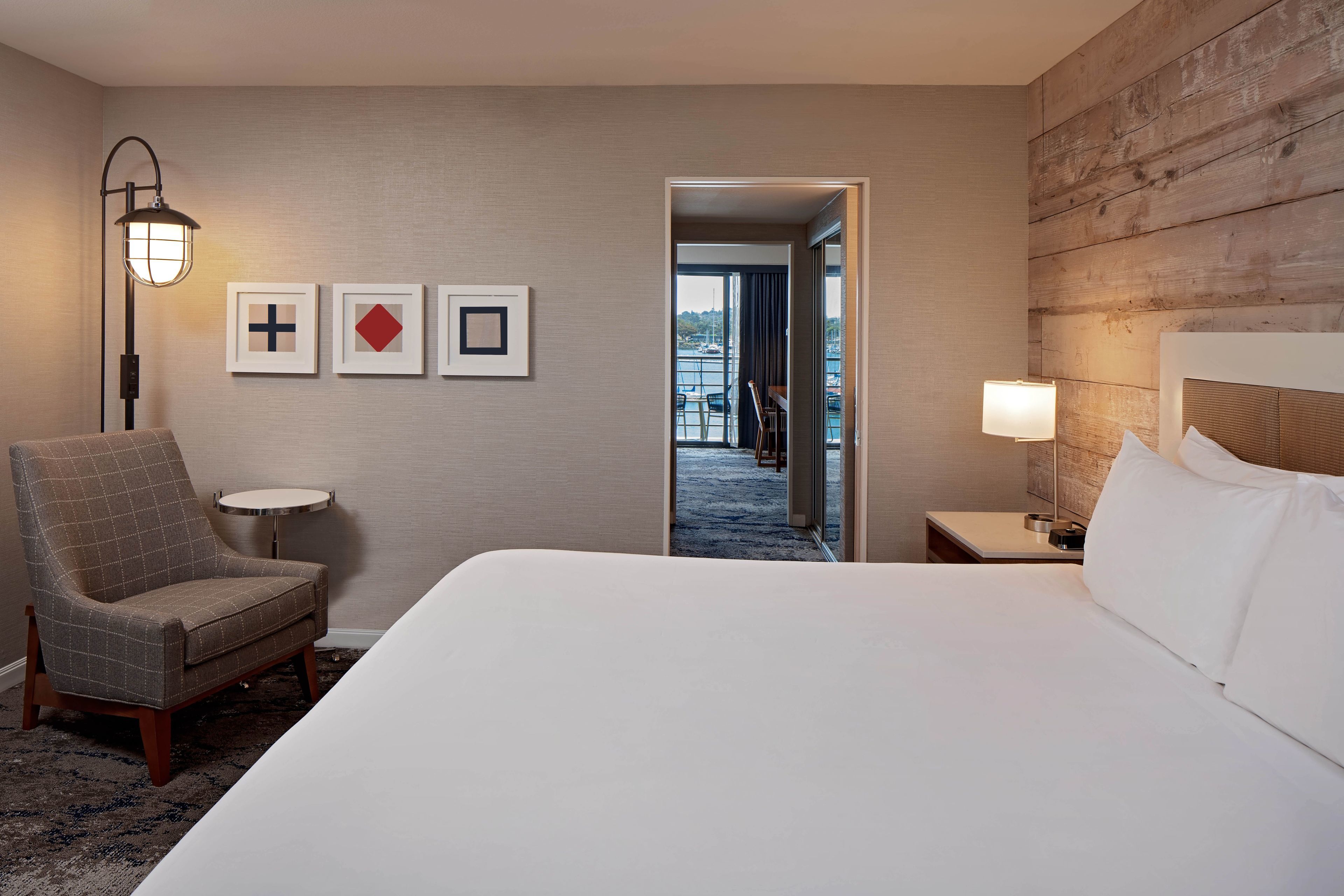 A hotel room with a large bed, a chair, a lamp, and framed pictures on the wall.
