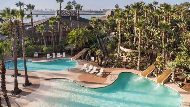 Una piscina de resort con un río lento, palmeras y vista al océano.