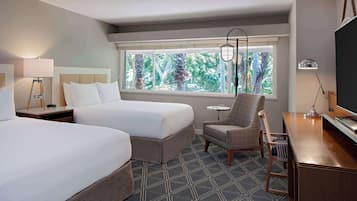 Une chambre d’hôtel avec deux lits, un bureau, une chaise, une lampe et une fenêtre donnant sur un paysage verdoyant.