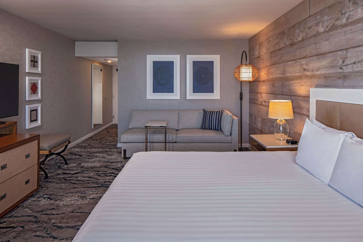 Una camera d'albergo con un letto grande, un divano, una scrivania, una TV e quadri appesi al muro.