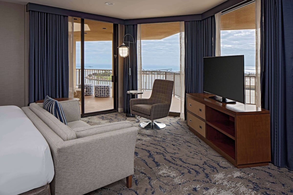 Una camera d'albergo con un letto, una poltrona, una sedia, una TV, una scrivania e vista sull'oceano.